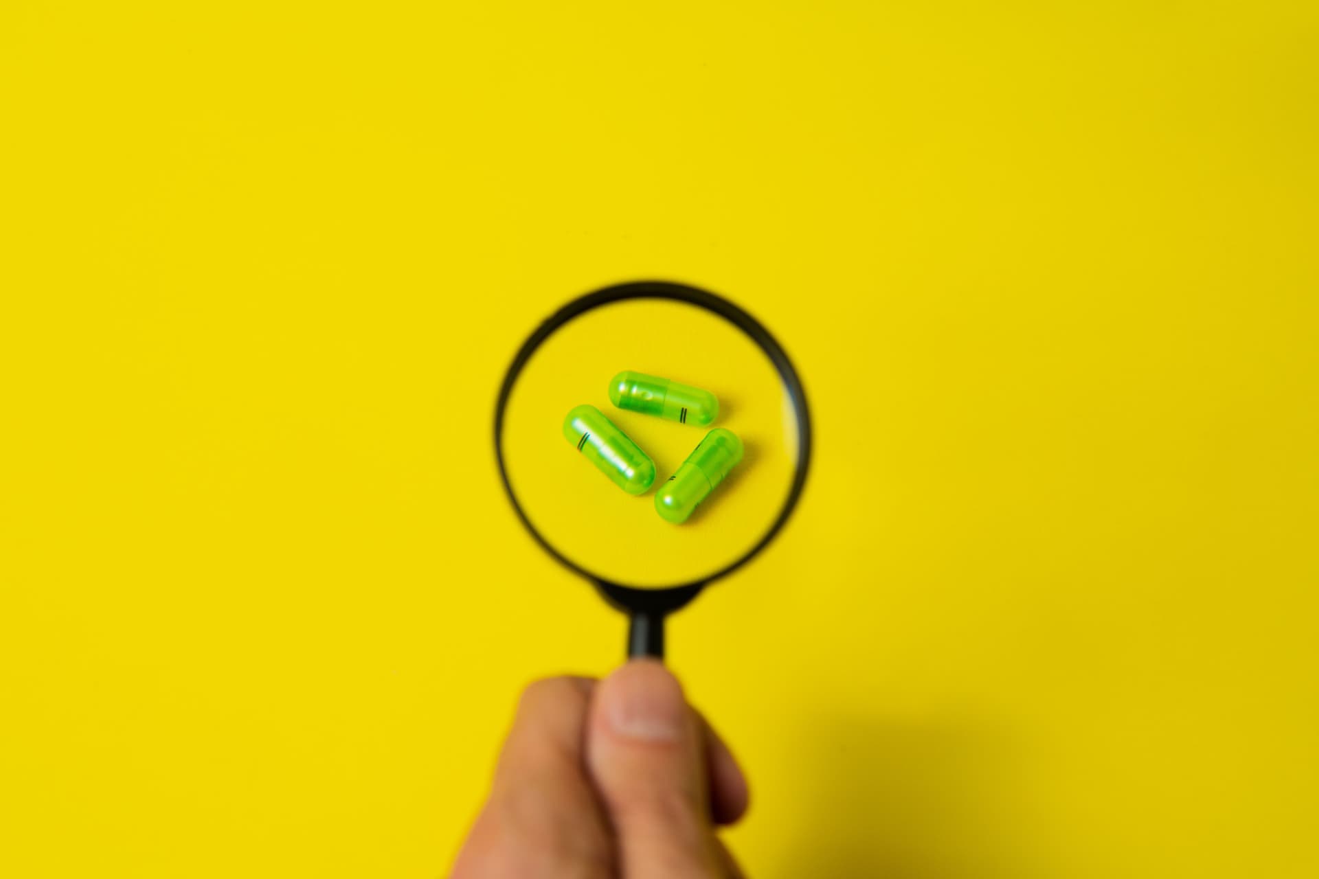 Close-up of green capsules magnified on a vibrant yellow background, symbolizing healthcare and research.