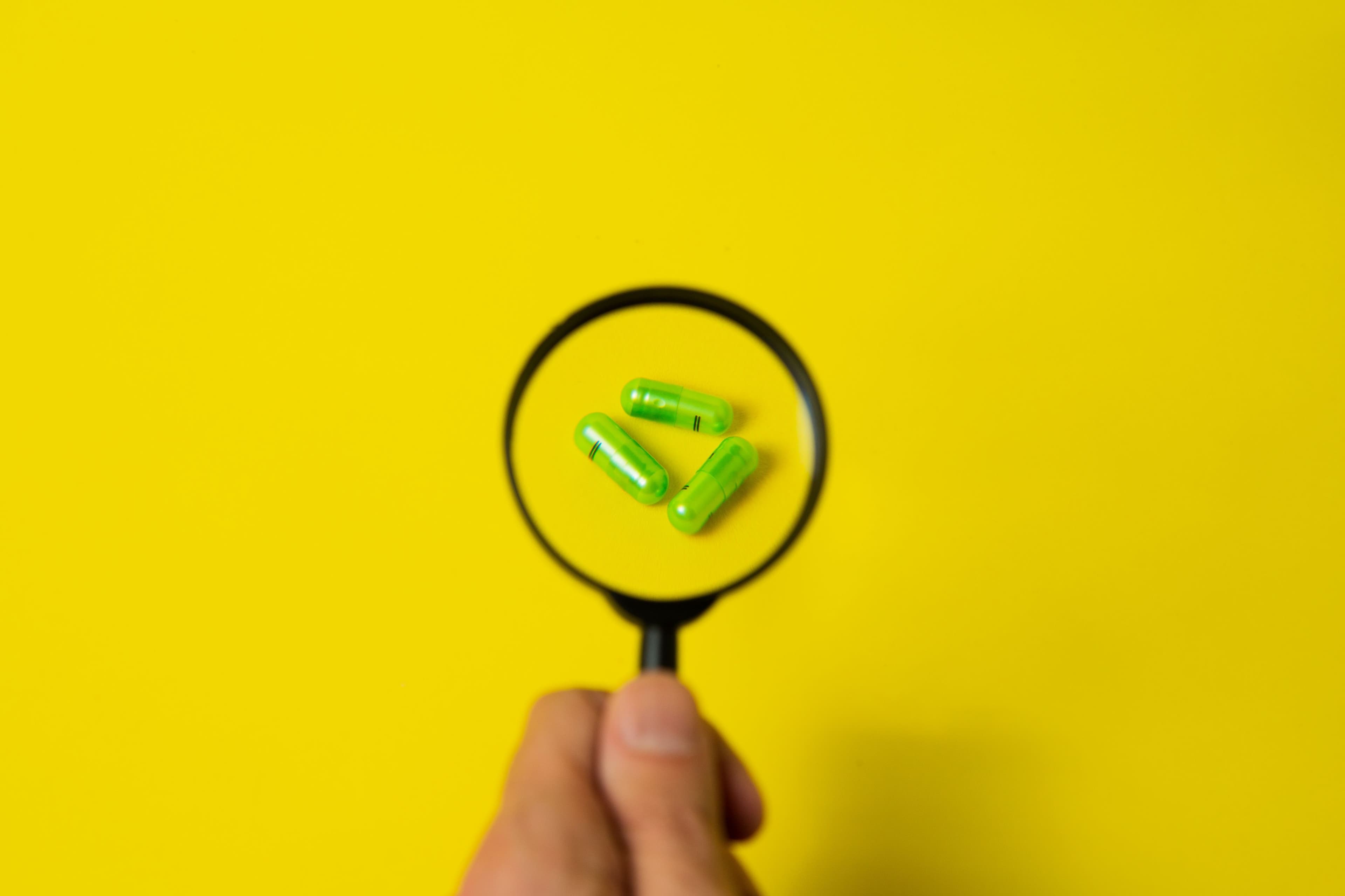 Close-up of green capsules magnified on a vibrant yellow background, symbolizing healthcare and research.