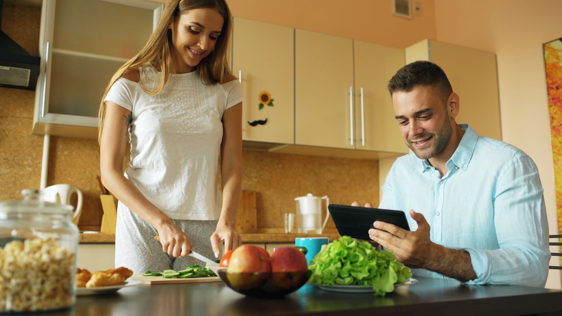 A man and woman happily preparing a healthy meal together in a modern kitchen setting.