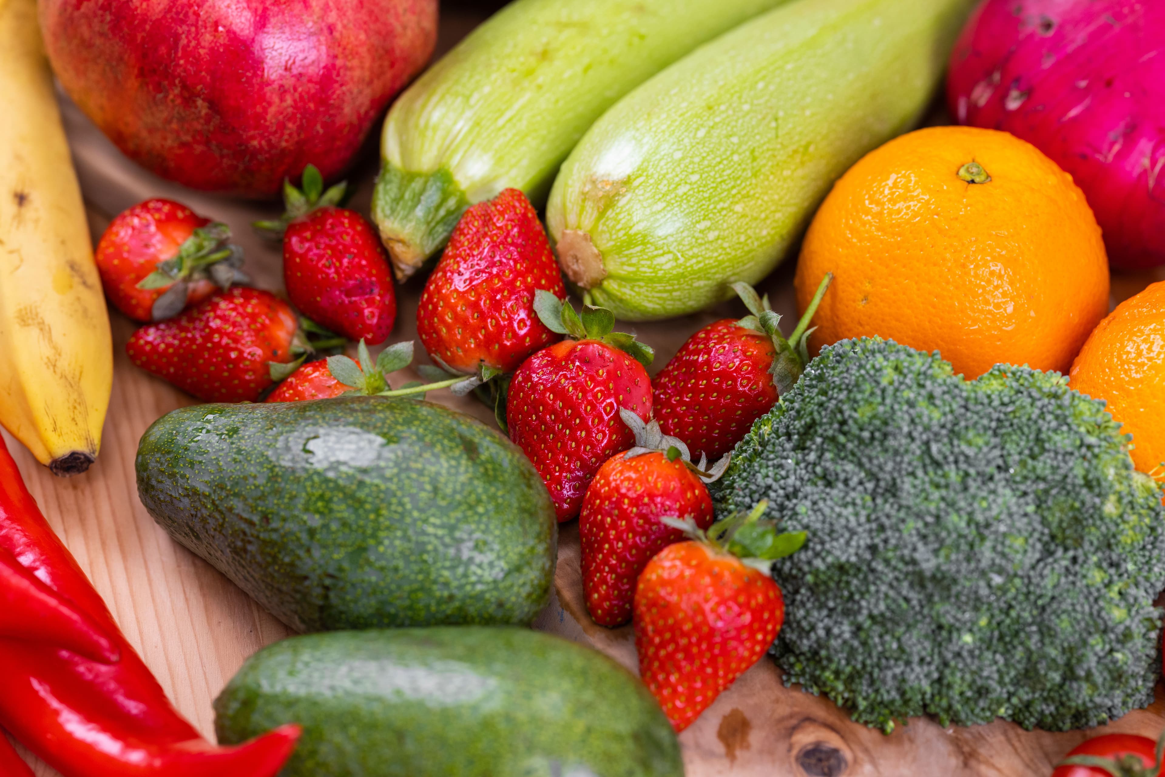 A vibrant selection of fresh fruits and vegetables including strawberries, avocado, and broccoli on a wooden table.