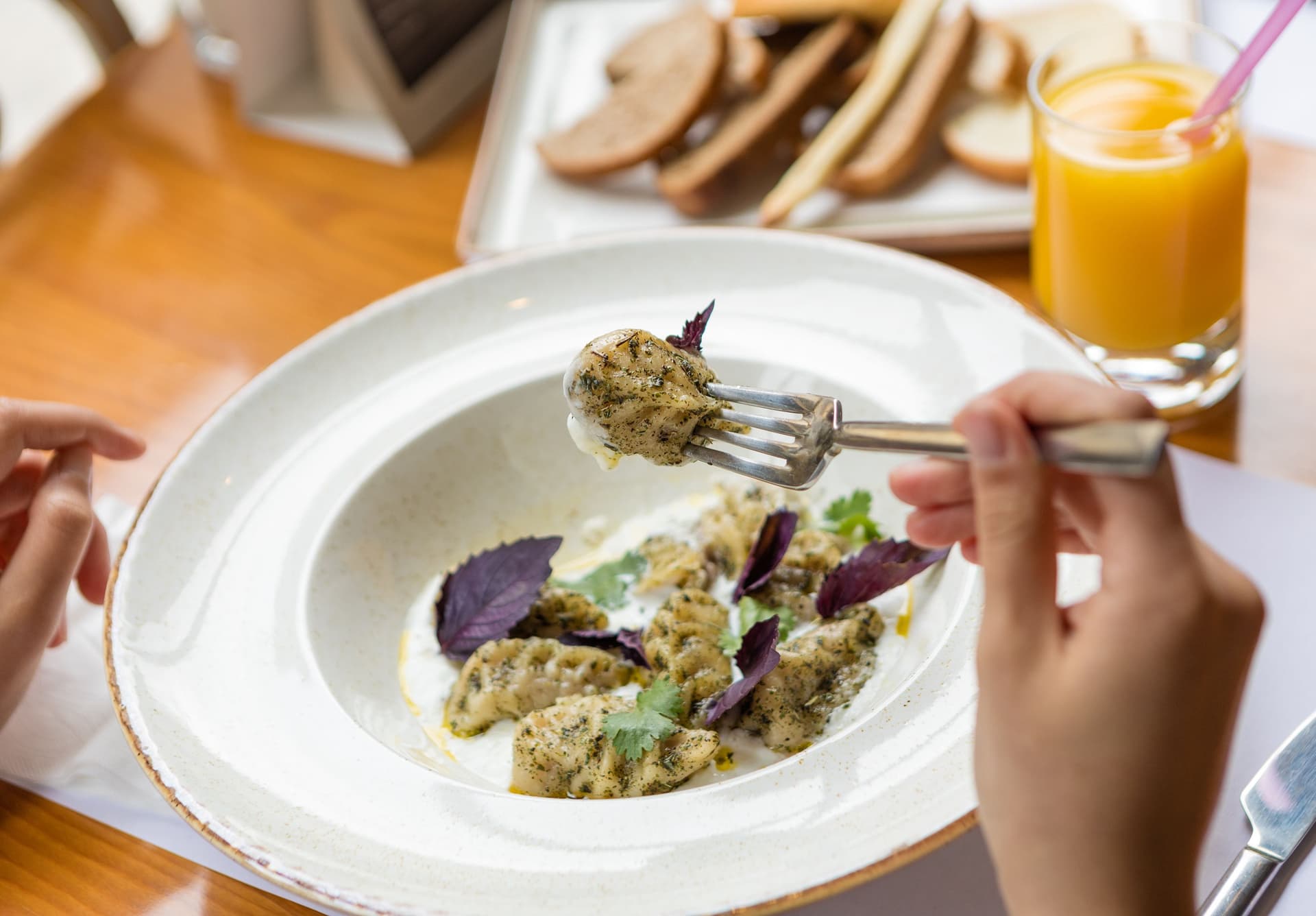 Savor a gourmet pasta dish garnished with fresh herbs, accompanied by juice and bread, on a wooden table.