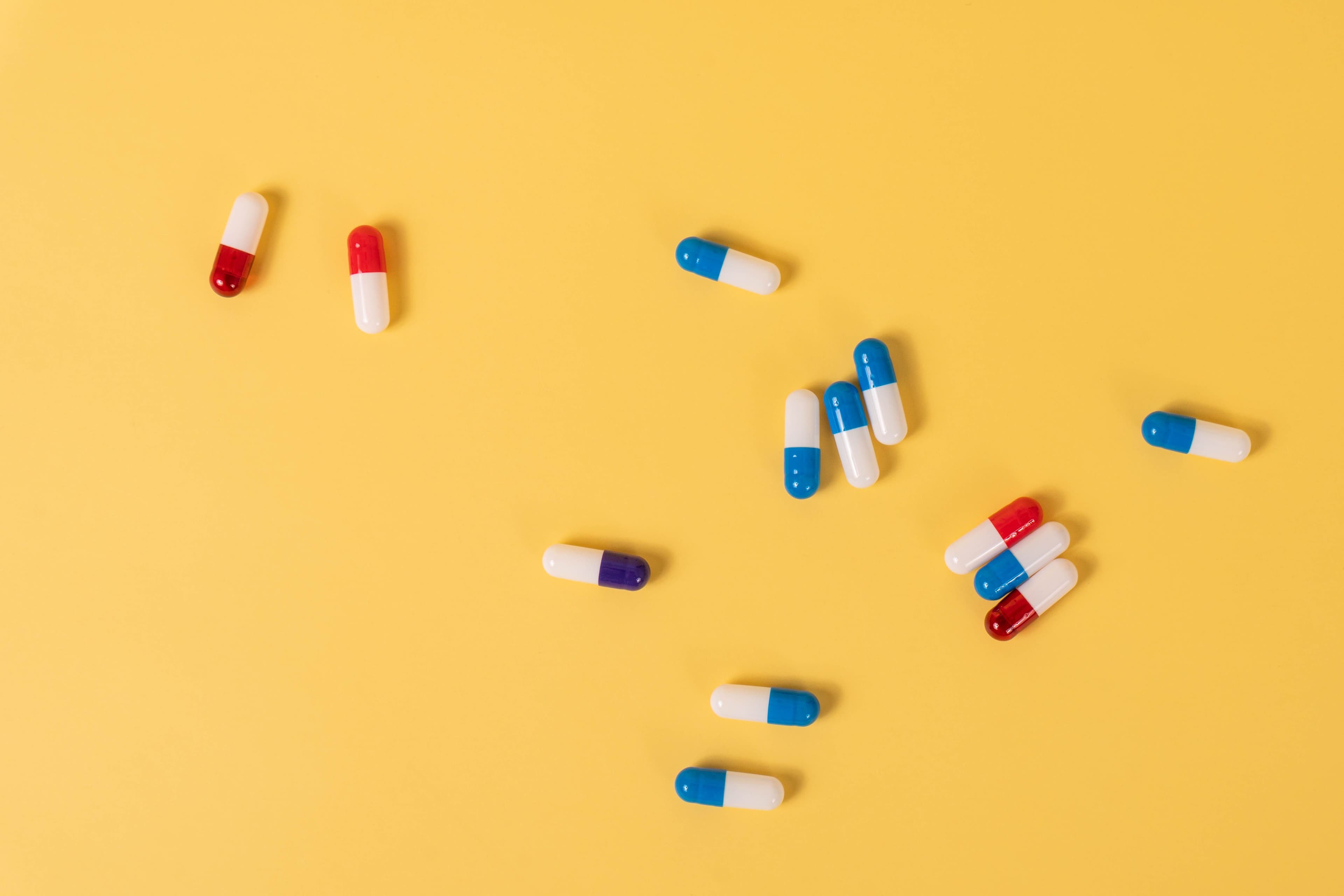 Colorful medication capsules scattered on a vivid yellow background, ideal for health-related themes.