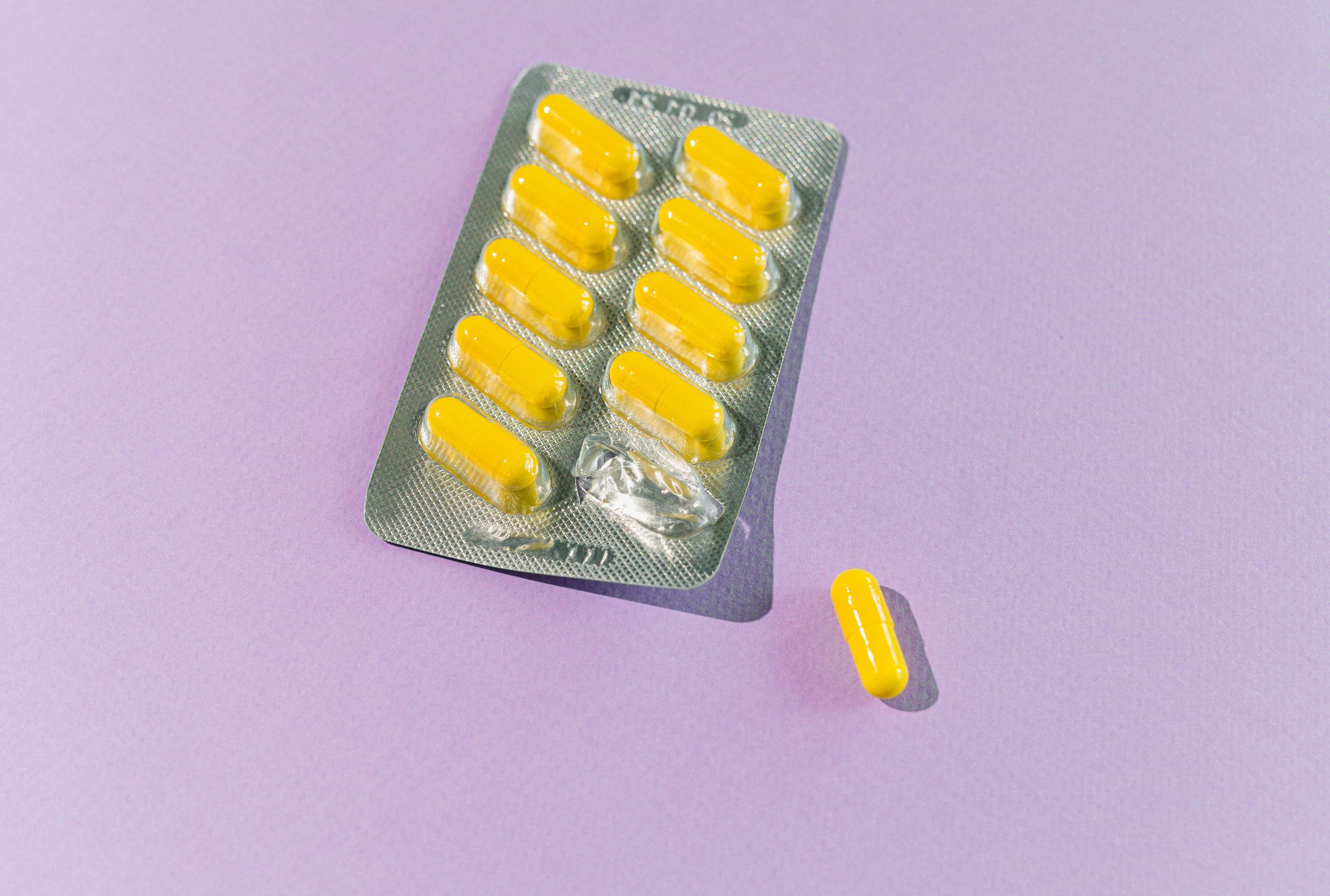 A blister pack of yellow capsules with one pill on a purple backdrop.