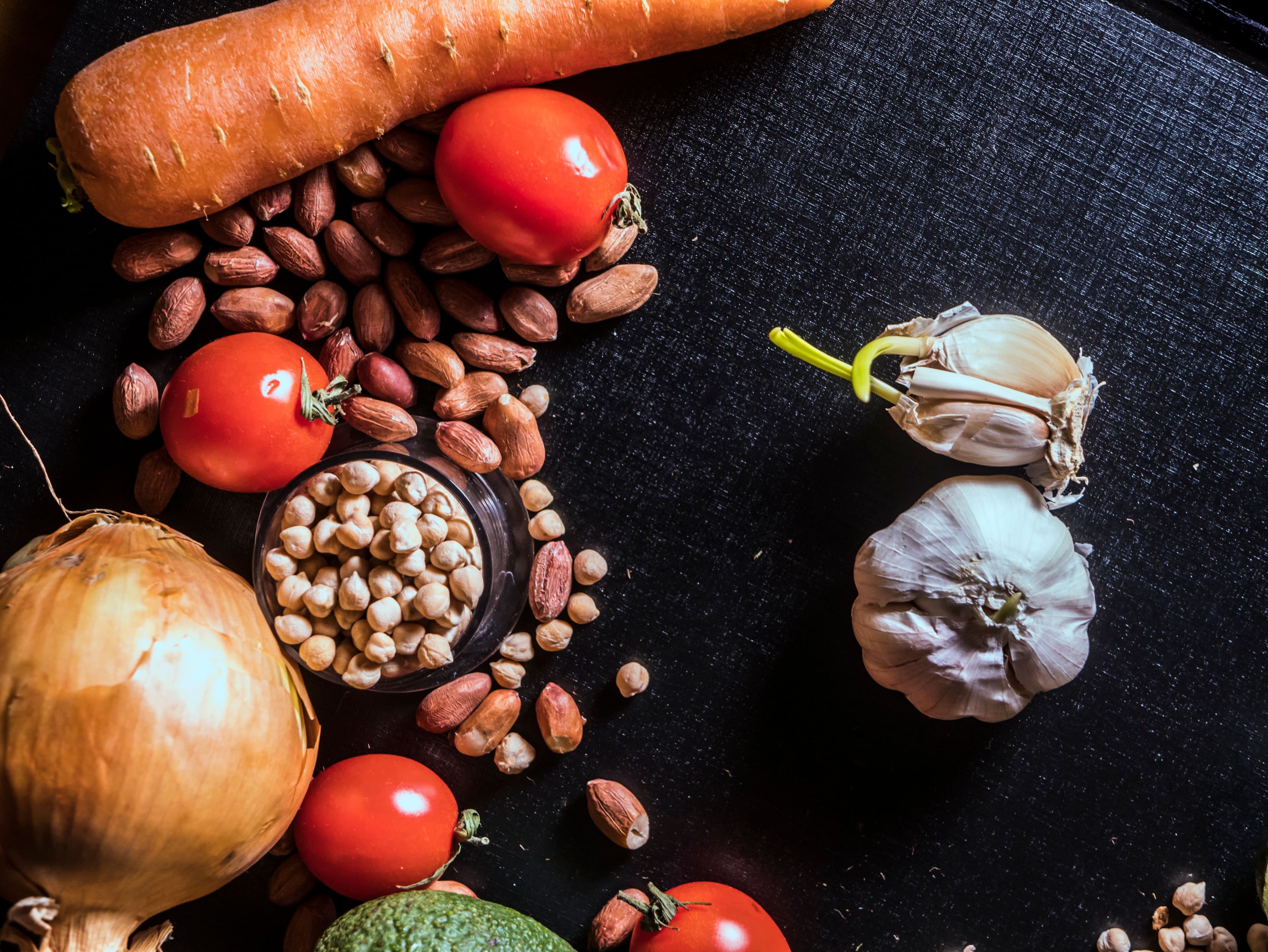 Top view of fresh vegetables and nuts arranged on a dark surface, showcasing raw ingredients.